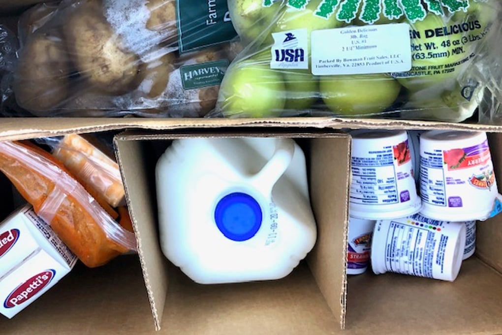 A box of fresh groceries (apples, potatoes, milk, eggs, and yogurt) packed at the food bank